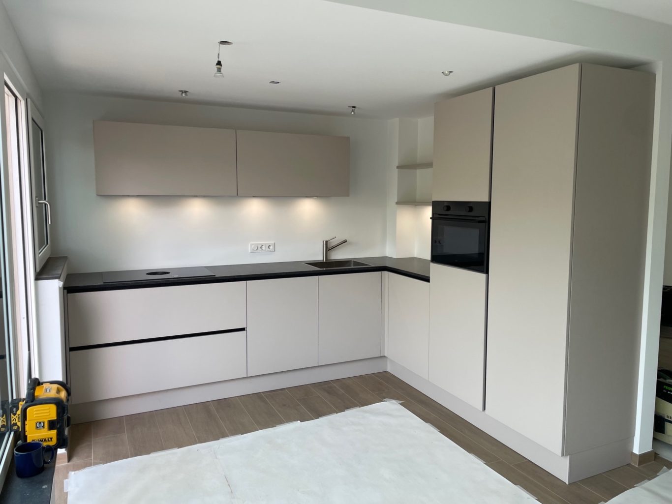 Moderne keuken met beige kasten, zwart aanrecht en ingebouwde apparatuur.